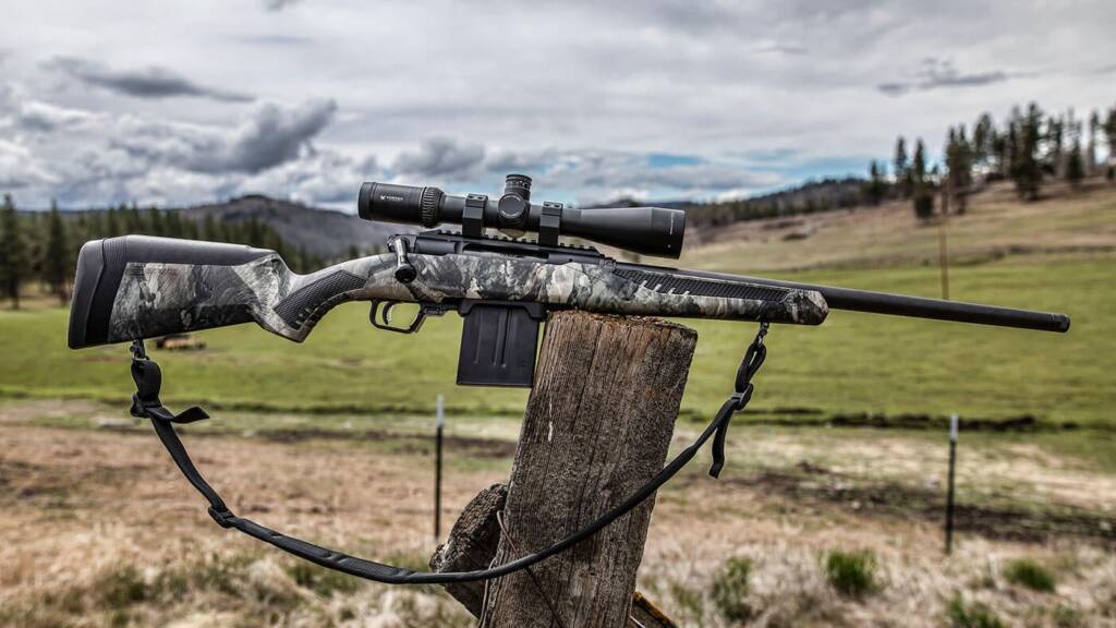 Bolt-action hunting rifle with a camo stock resting on a fence post