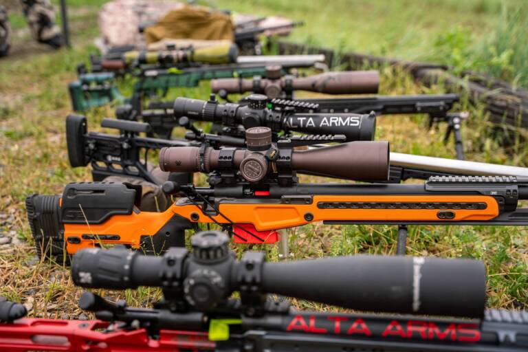 Row of precision rifles with Alta Arms chassis and large scopes on the grass